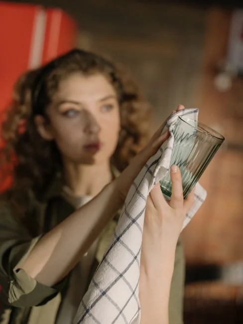 A woman cleans a mirror indoors using a blue cloth, reflecting cleanliness and home care.